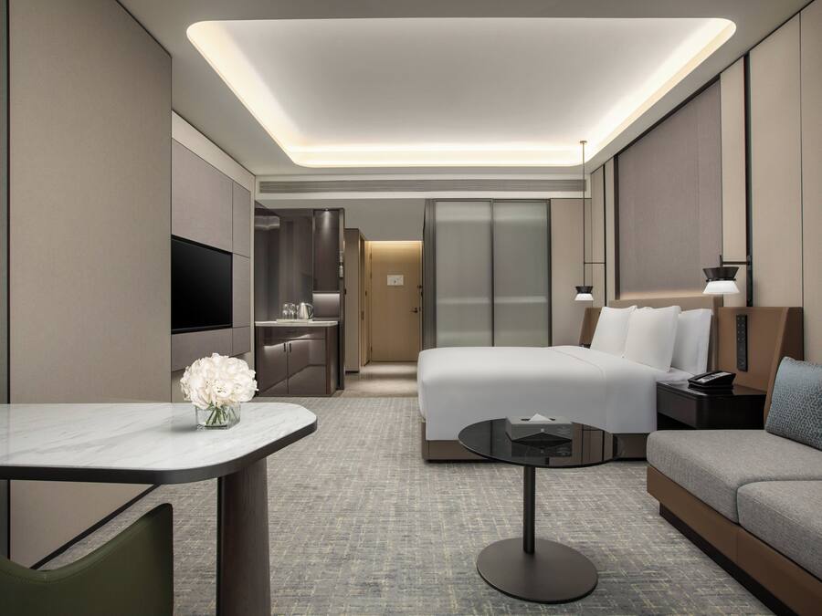 Quarto de hotel moderno com cama, sofá, escrivaninha e televisão.