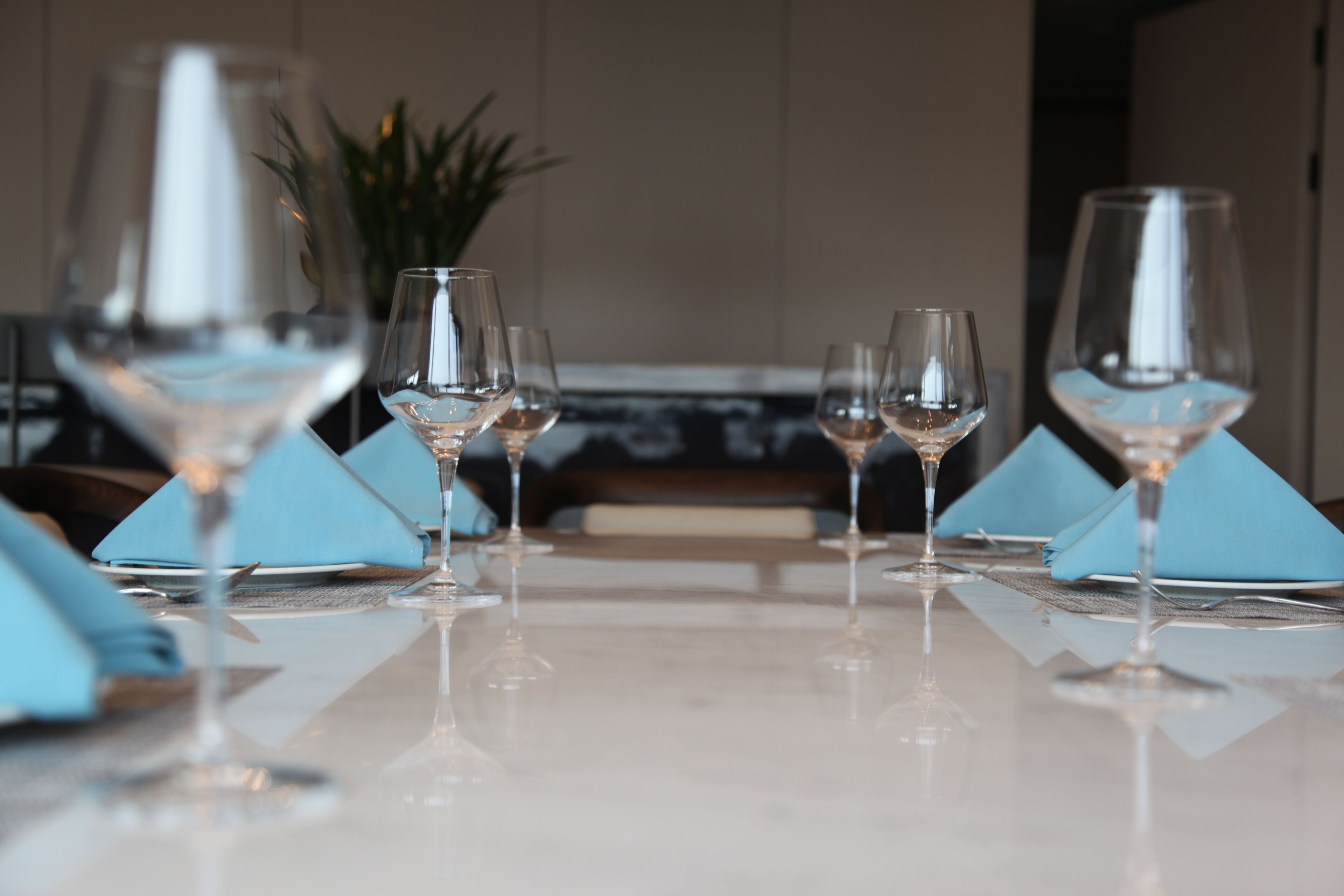 Une table dressée avec des verres à vin et des serviettes bleues.
