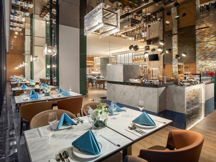 Un restaurant moderne avec des tables en marbre, des serviettes bleues et des luminaires suspendus.