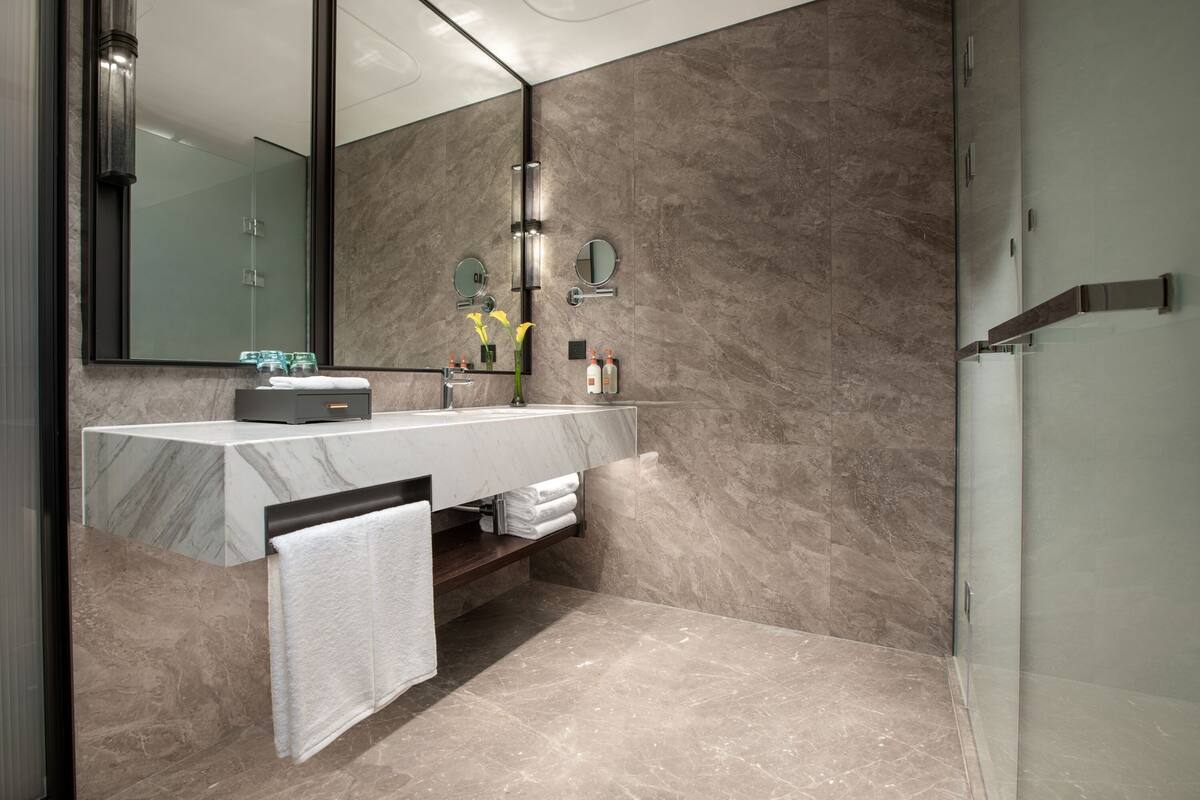 Een moderne badkamer met een marmeren wastafelblad, een grote spiegel en een douchecabine met glazen wanden.