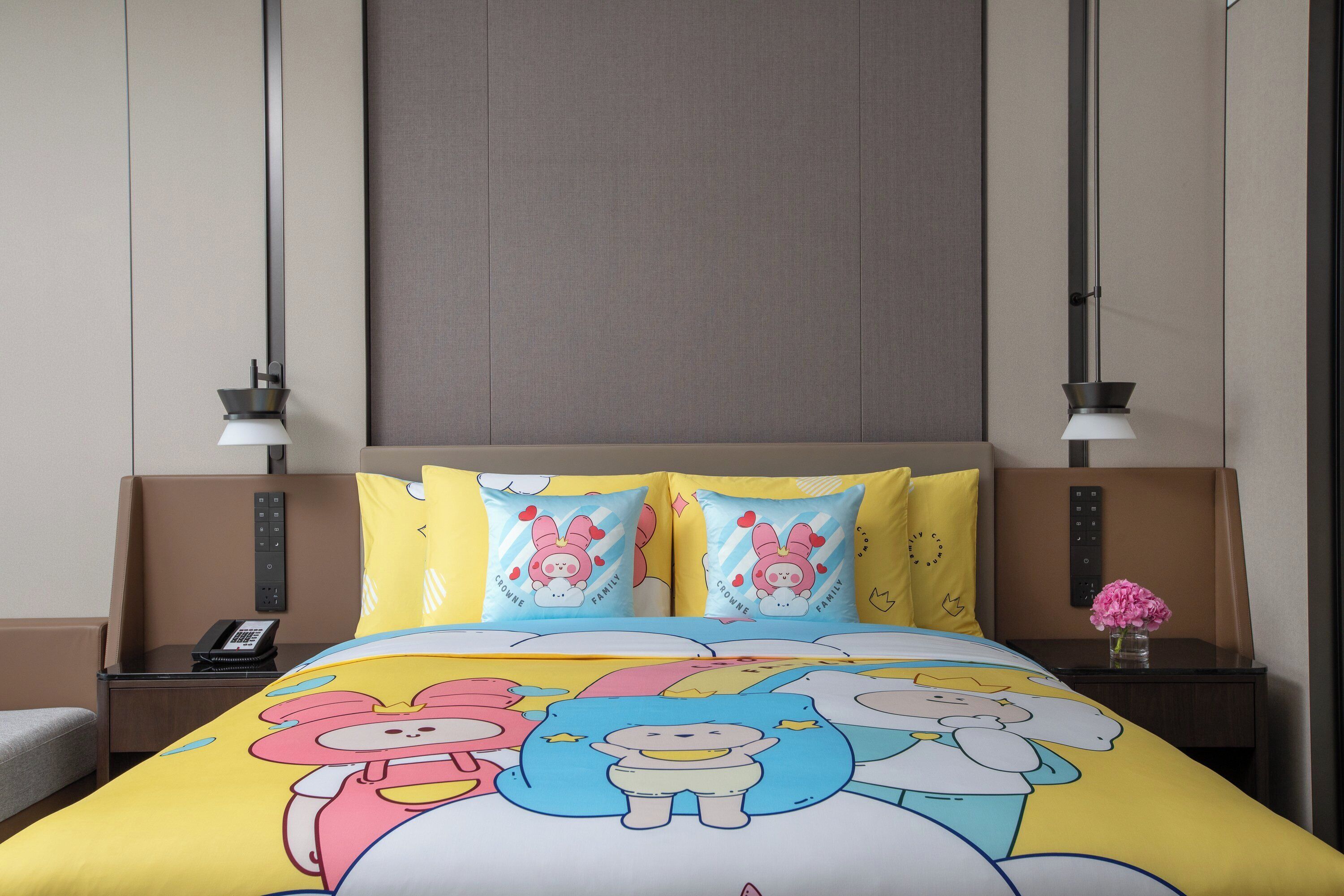 A hotel room with a bed, bedside tables, a nightstand, a lamp, and a vase with flowers.