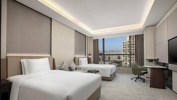 Une chambre d’hôtel avec deux lits, un bureau, une chaise et une grande fenêtre donnant sur la ville.