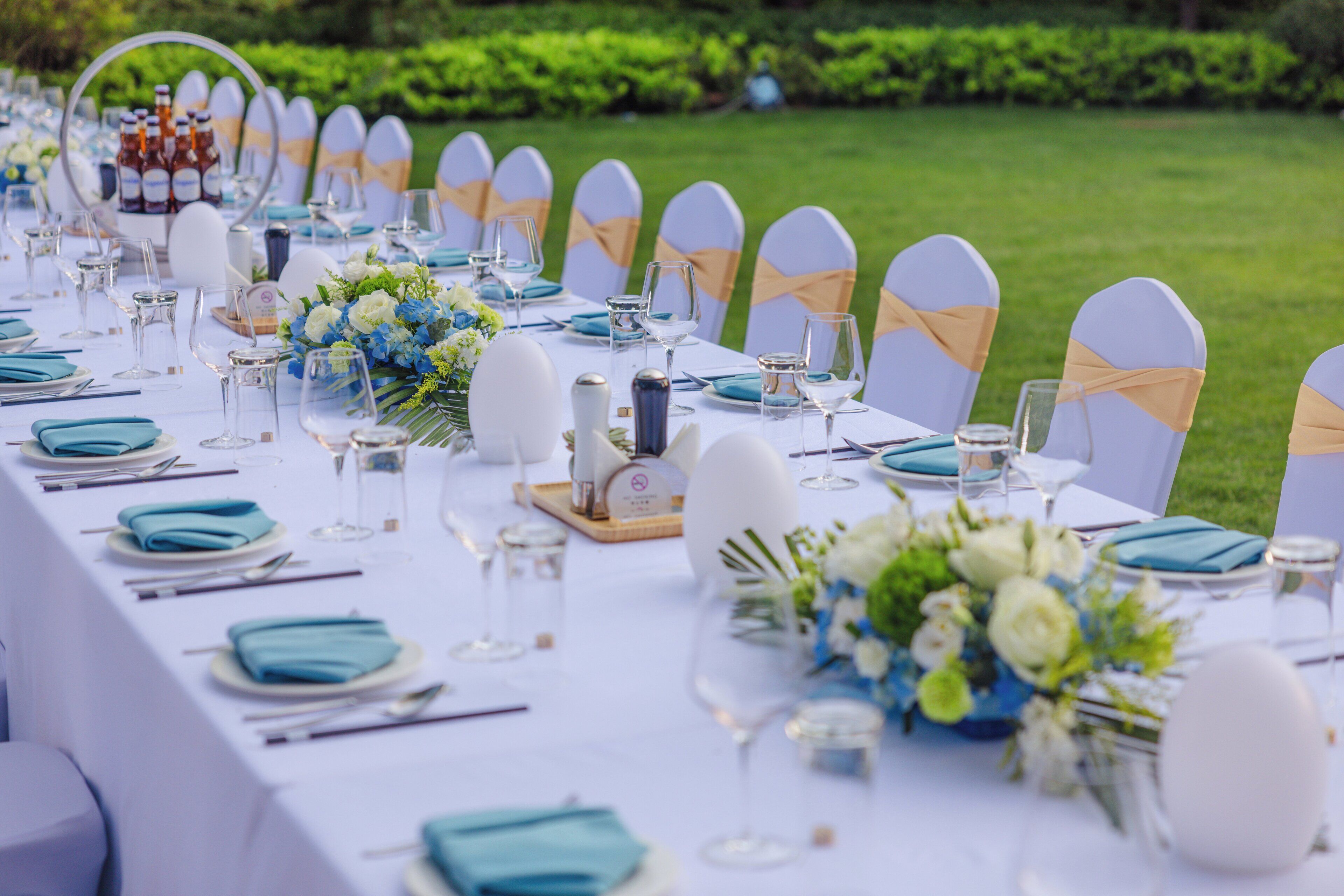 A long dining table set with white and blue tableware, glassware, and floral centerpieces.