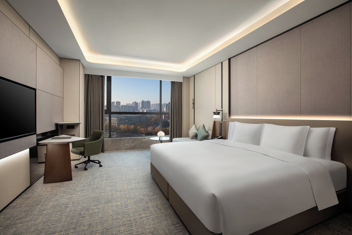 Une chambre d’hôtel moderne dotée d’un grand lit, d’un bureau, d’une chaise, d’une télévision et offrant une vue sur le paysage urbain.