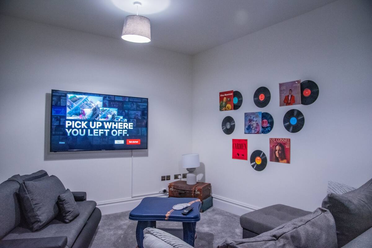 A modern living room with a flat-screen TV, grey sofas, a coffee table, and vinyl records on the wall.