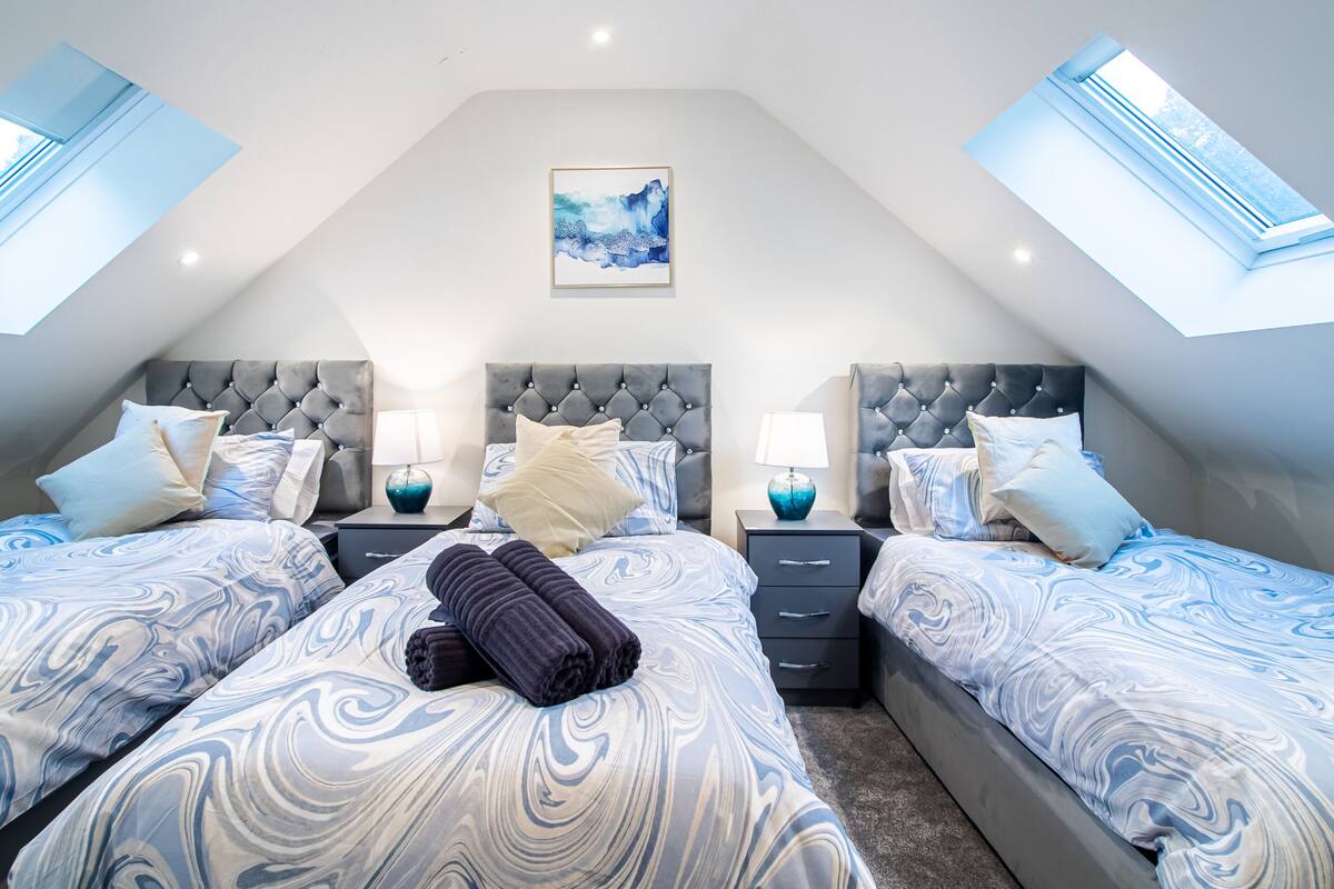 A bedroom with three beds, each with a marble-patterned bedspread, two bedside tables with lamps, and a ceiling skylight.