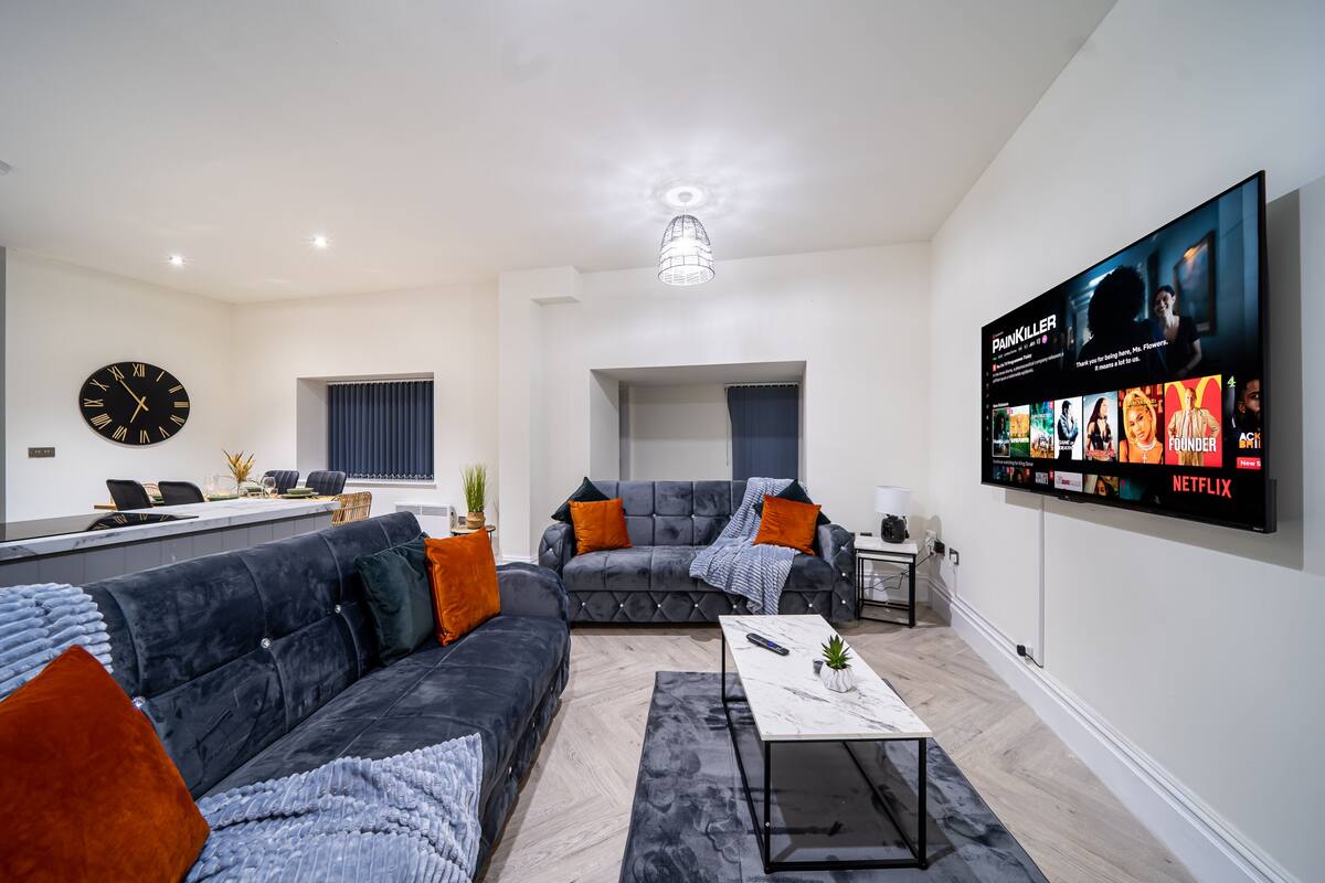 A modern living room with a grey sofa, a coffee table, and a TV mounted on the wall displaying a Netflix interface.