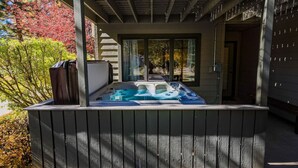 Un bain à remous situé dans un espace extérieur abrité, doté d’une terrasse en bois et offrant une vue sur un jardin aux couleurs automnales.