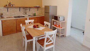 A compact kitchen with a wooden table and chairs, a microwave, and a refrigerator. - Two-roomed house "In centro" + services in the baroque heart of the city (Noto)