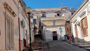 A narrow cobblestone street flanked by historic buildings with traditional architecture, including a staircase leading to a higher level. - Two-roomed house "In centro" + services in the baroque heart of the city (Noto)
