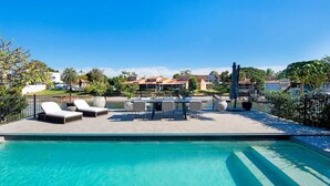 A swimming pool with lounge chairs and a table, surrounded by a fence and greenery. - Capri Waterfront Oasis Pool, 4bd steps to Surfers (Gold Coast)