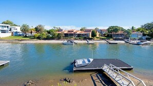 A marina with several boats docked, a dock with a boat ramp, and modern houses in the background. - Capri Waterfront Oasis Pool, 4bd steps to Surfers (Gold Coast)