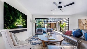 A modern living room with a large painting, a ceiling fan, and a view of the outdoors. - Capri Waterfront Oasis Pool, 4bd steps to Surfers (Gold Coast)