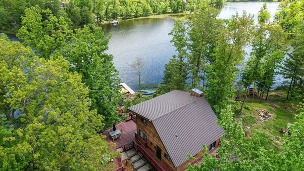 A cabin with a sloped roof, surrounded by dense forest and a lake. - Waterfront Cabin on Long Lake w/ Dock & Kayaks! (Comstock)