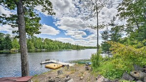 A lakeside campsite with a dock, picnic tables, and scattered logs. - Waterfront Cabin on Long Lake w/ Dock & Kayaks! (Comstock)