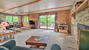 A log cabin interior with a fireplace, wooden furniture, and a stone wall. - Waterfront Cabin on Long Lake w/ Dock & Kayaks! (Comstock)