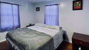 A bedroom with a bed, two nightstands, a wooden dresser, and a ceiling light.