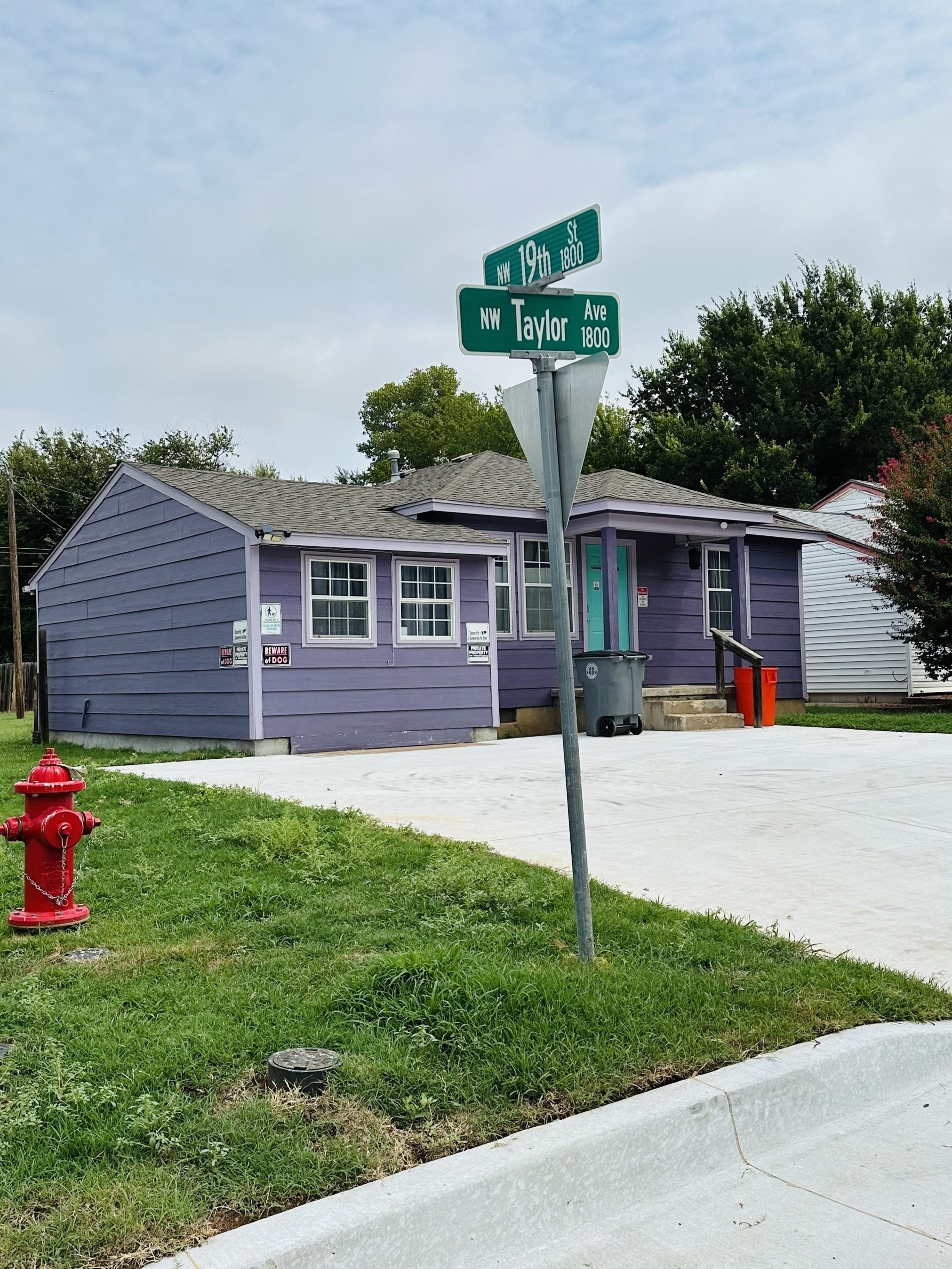 A small, single-story building with a purple exterior and a green sign indicating it is located at NW 19th St and NW Taylor Ave.