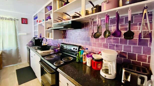 A kitchen with a stove, oven, and various kitchen utensils on shelves.