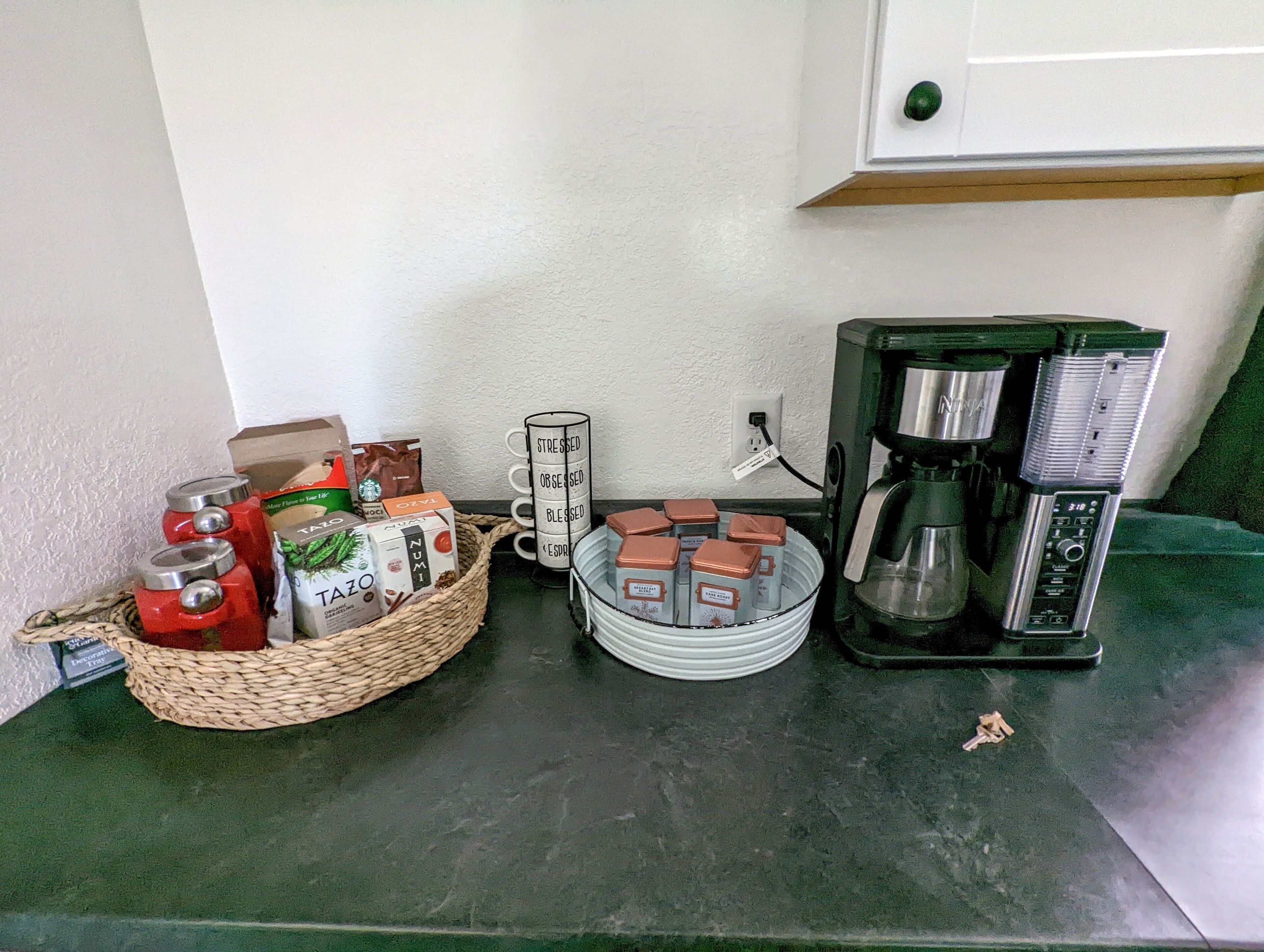 A kitchen counter with a coffee maker, a basket of tea bags, and a mug with motivational phrases.