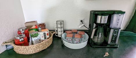 A kitchen counter with a coffee maker, a basket of tea bags, and a mug with motivational phrases.