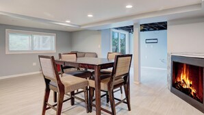 Uma sala de jantar com mesa e cadeiras de madeira, lareira e vista para o exterior pela janela.
