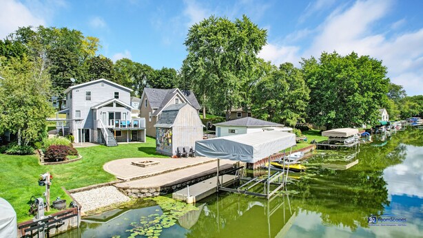 Uma propriedade à beira do lago com um cais, um barco coberto e uma casa grande com terraço.