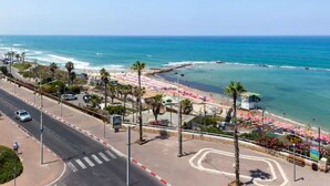Eine Küstenstraße mit einem Strand zur Rechten, mit Fußgängerweg und parkenden Autos.