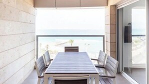 Ein Balkon mit Tisch und Stühlen, Blick auf den Strand und eine Glastür zum Innenbereich.