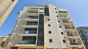A multi-story residential building with balconies, a central stairwell, and a clear sky. - O&O Group - Deluxe Beachfront 3 BR Penthouse (Bat Yam)