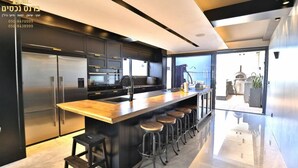 A modern kitchen with a central island, stainless steel appliances, and bar stools. - O&O Group - Deluxe Beachfront 3 BR Penthouse (Bat Yam)