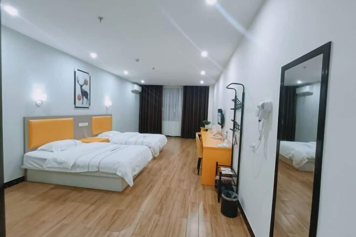 A hotel room with two beds, a desk, a chair, a mirror, and a waste bin.