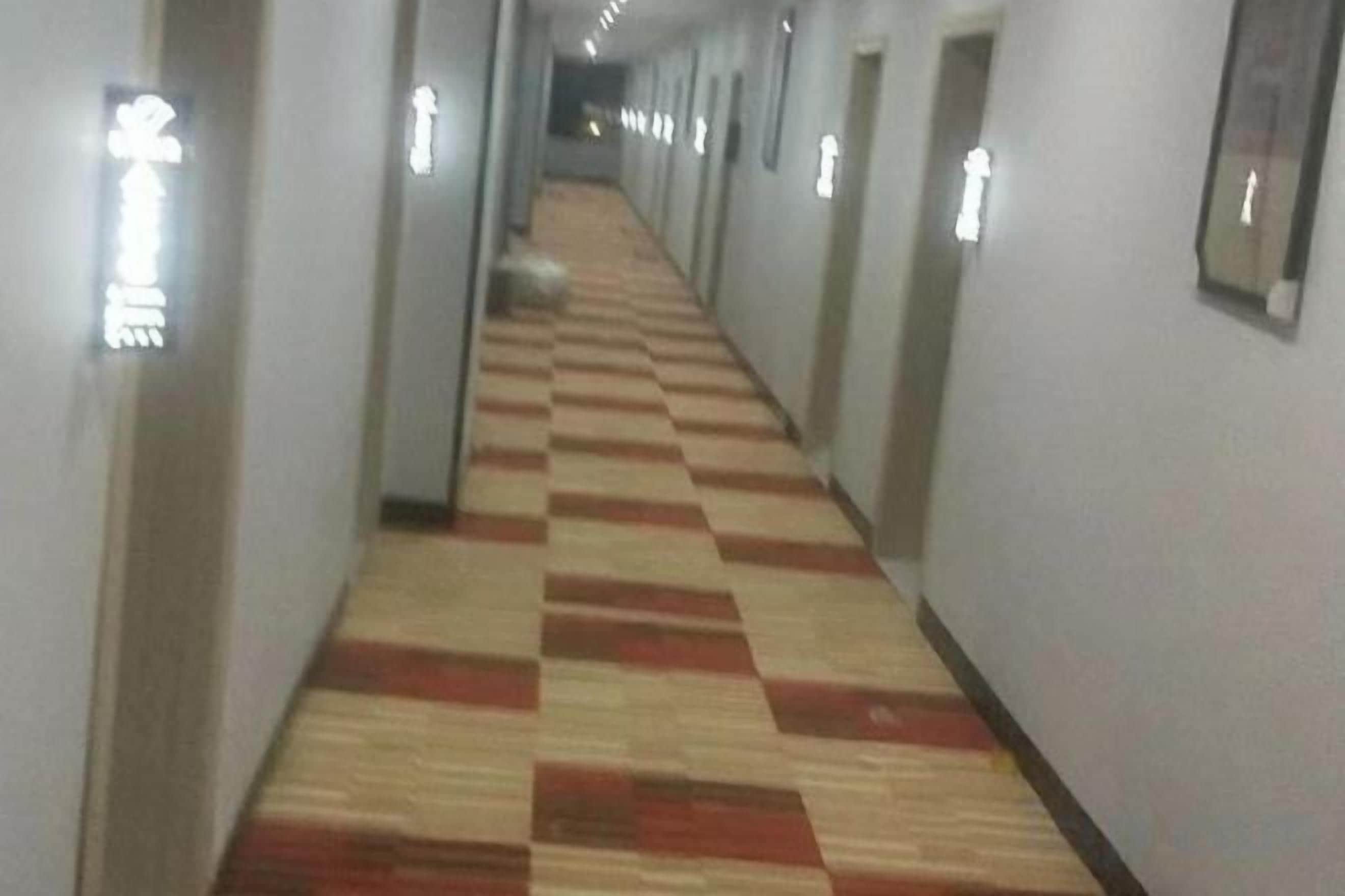 A long hallway with a checkered carpet and light fixtures on the walls.
