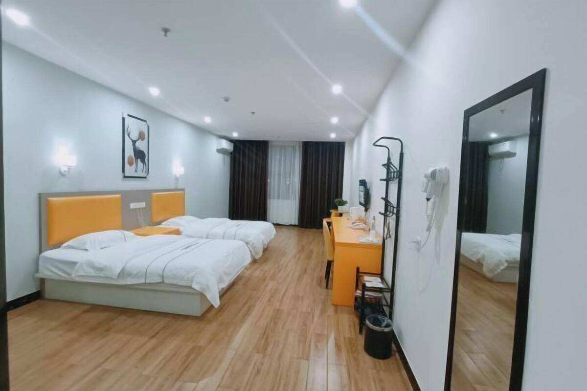 A hotel room with two beds, a desk, a mirror, and a ceiling light.