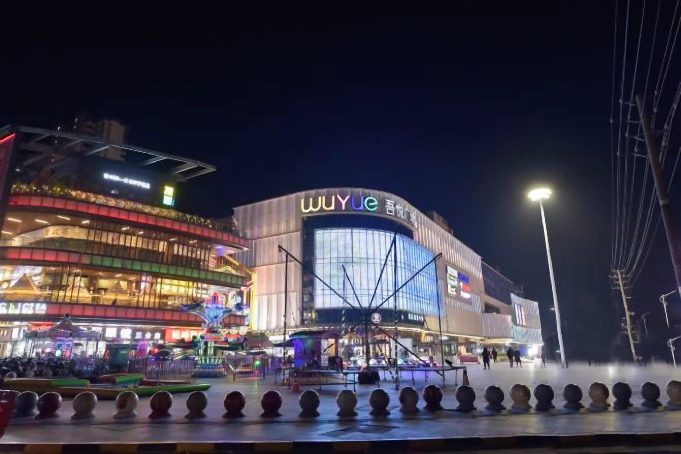 A modern building with a prominent signage, a public square with a fountain, and a well-lit street.