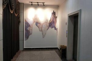 Um corredor com uma grande obra de arte abstrata na parede, uma porta à direita e uma pequena mesa com uma cadeira.