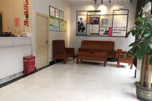 A reception area with a reception desk, wooden seating, a potted plant, and informational posters on the wall. - Qinji Hotel (Wuyue Plaza Baishihu Park) (Qinzhou)