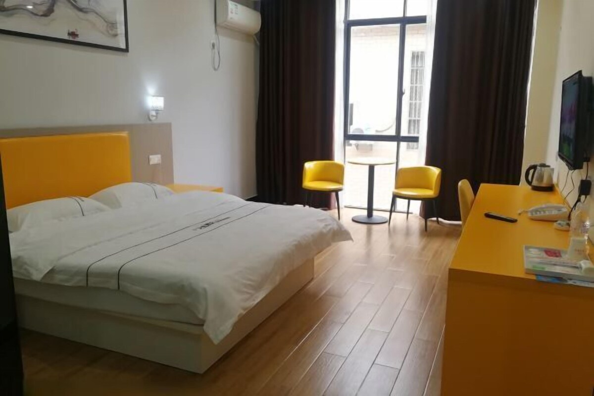 Una camera d'albergo con un letto, una scrivania, due sedie, una televisione e una finestra con tende.