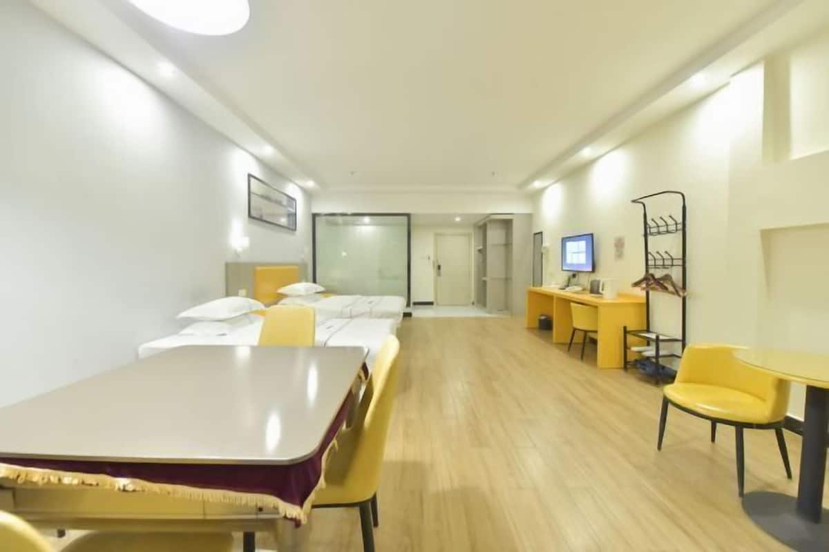 A hotel room with a bed, a desk, a chair, a TV, and a shelf with items.
