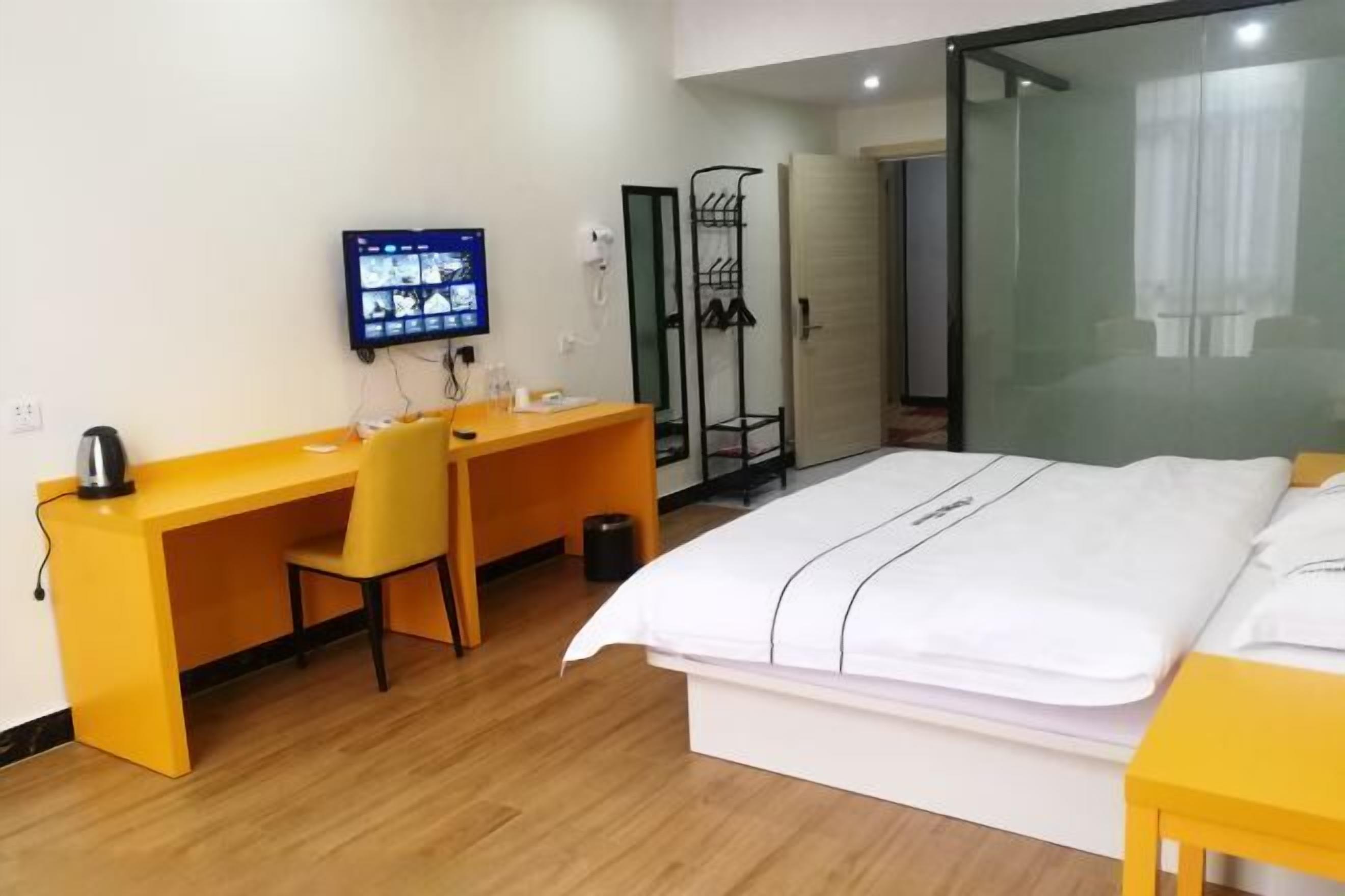 A hotel room with a bed, a desk, a chair, a TV, and a wardrobe.