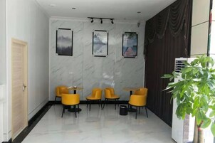 A hotel lobby with a marble wall, framed pictures, yellow chairs, and a potted plant.