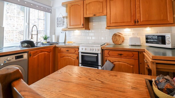 A kitchen with wooden cabinets, a microwave, a stove, and a dishwasher. - Honeybee Cottage (Ripon)