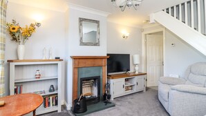 A living room with a fireplace, television, bookshelf, and a grey armchair. - Honeybee Cottage (Ripon)
