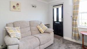 A living room with a grey sofa, two plaid cushions, a floral painting, a black door, and a window with plaid curtains. - Honeybee Cottage (Ripon)