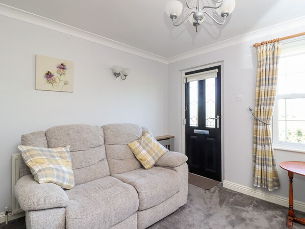 A living room with a grey sofa, two plaid cushions, a floral painting, a black door, and a window with plaid curtains.