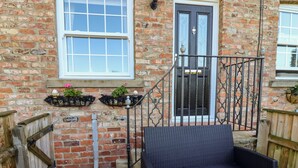 A brick house with a black door, white windows, and a wooden deck. - Honeybee Cottage (Ripon)