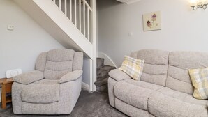 A living room with a staircase, two armchairs, a sofa, and a wall-mounted light fixture. - Honeybee Cottage (Ripon)