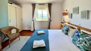 Ein Hotelzimmer mit Bett, Stuhl, Nachttisch und einem Fenster mit Vorhängen.