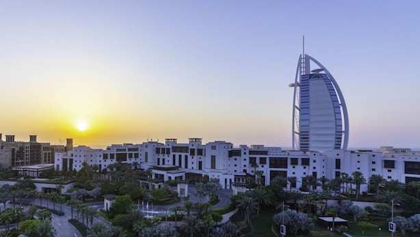 A modern hotel complex with a distinctive sail-shaped building, surrounded by lush greenery and a clear sky. - Maison Privee - Exclusive Luxury 3BR Apt with scenic views of Burj Al Arab (Dubai)