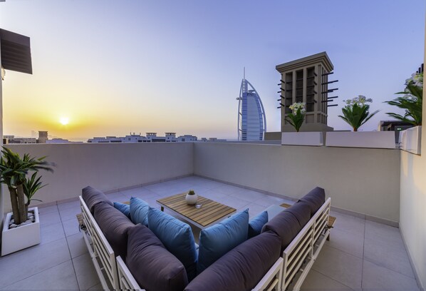 Eine Dachterrasse mit Sitzgelegenheit, Blick auf den Burj Al Arab und einem modernen Gebäude im Hintergrund.